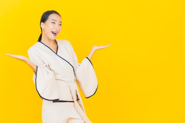Retrato de joven y bella mujer asiática de negocios sonriendo con traje blanco en la pared amarilla