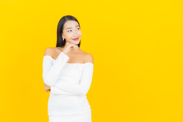 Retrato de joven y bella mujer asiática de negocios sonriendo con vestido blanco en la pared amarilla