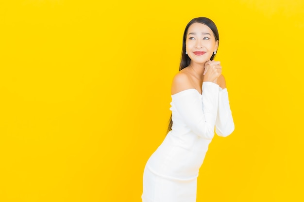 Retrato de joven y bella mujer asiática de negocios sonriendo con vestido blanco en la pared amarilla