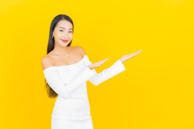 Retrato de joven y bella mujer asiática de negocios sonriendo con vestido blanco en la pared amarilla