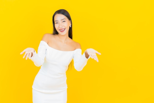 Retrato de joven y bella mujer asiática de negocios sonriendo con vestido blanco en la pared amarilla