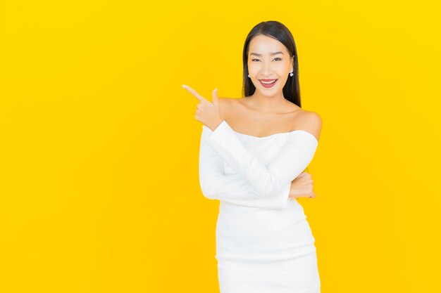 Retrato de joven y bella mujer asiática de negocios sonriendo con vestido blanco en la pared amarilla