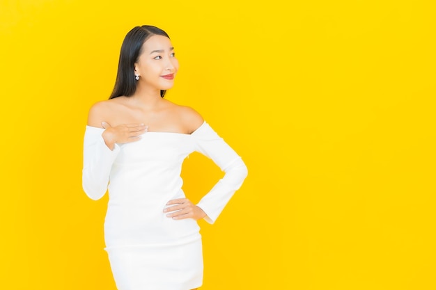 Retrato de joven y bella mujer asiática de negocios sonriendo con vestido blanco en la pared amarilla