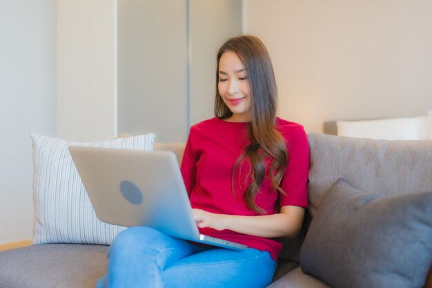 Retrato joven y bella mujer asiática con ordenador portátil en el sofá en el salón