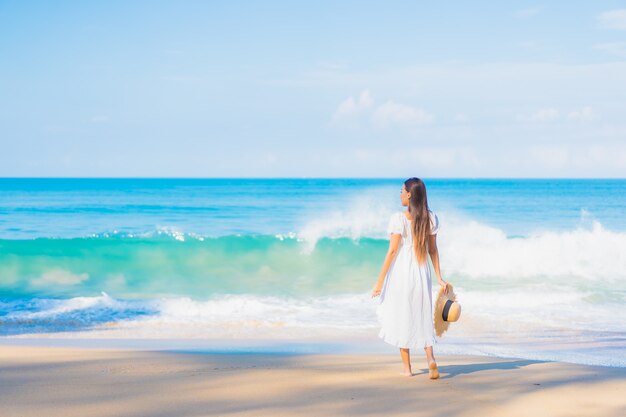 Retrato de joven y bella mujer asiática relajándose en la playa con nubes blancas en el cielo azul en viajes de vacaciones