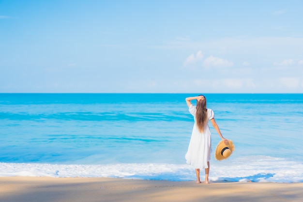 Retrato de joven y bella mujer asiática relajándose en la playa con nubes blancas en el cielo azul en viajes de vacaciones