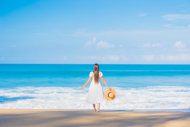 Retrato de joven y bella mujer asiática relajándose en la playa con nubes blancas en el cielo azul en viajes de vacaciones