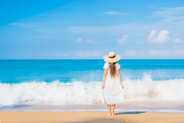 Retrato de joven y bella mujer asiática relajándose en la playa con nubes blancas en el cielo azul en viajes de vacaciones