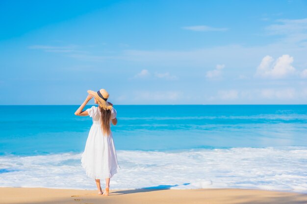 Retrato de joven y bella mujer asiática relajándose en la playa con nubes blancas en el cielo azul en viajes de vacaciones