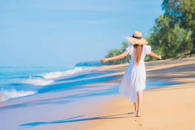 Retrato de joven y bella mujer asiática relajándose en la playa con nubes blancas en el cielo azul en viajes de vacaciones