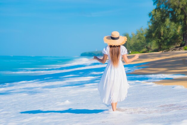 Retrato de joven y bella mujer asiática relajándose en la playa con nubes blancas en el cielo azul en viajes de vacaciones