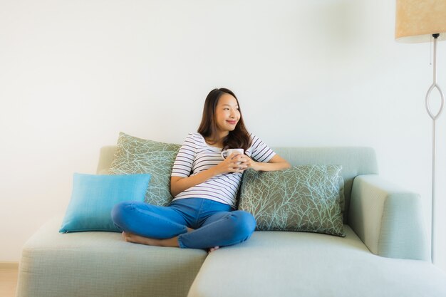 Retrato joven y bella mujer asiática en el sofá con una taza de café
