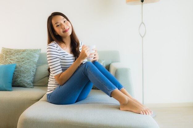 Retrato joven y bella mujer asiática en el sofá con una taza de café