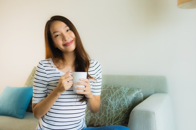 Retrato joven y bella mujer asiática en el sofá con una taza de café