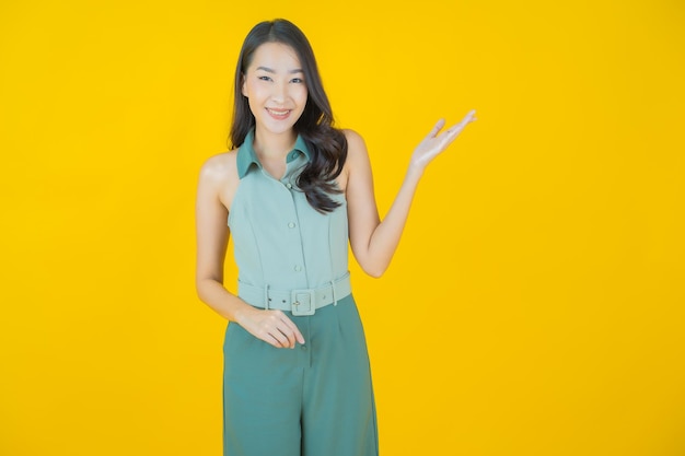 Retrato de joven y bella mujer asiática sonríe haciendo acción en la pared amarilla