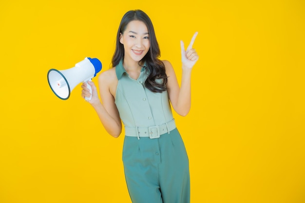 Retrato de joven y bella mujer asiática sonríe con megáfono en la pared amarilla