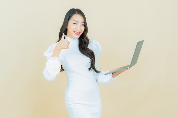 Retrato de joven y bella mujer asiática sonríe con ordenador portátil en la pared aislada