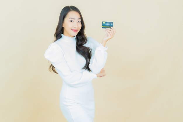 Retrato de joven y bella mujer asiática sonríe con tarjeta de crédito en la pared de color