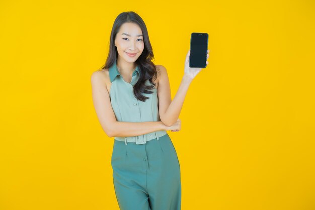 Retrato de joven y bella mujer asiática sonríe con teléfono móvil inteligente en la pared amarilla