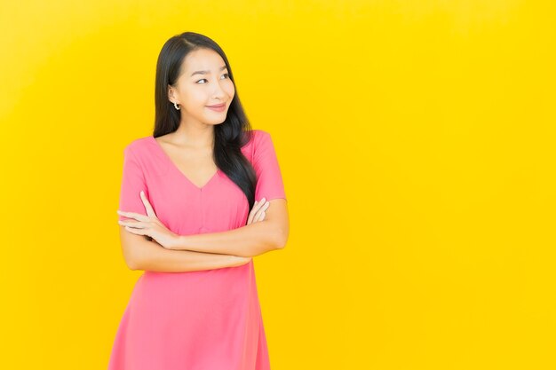 Retrato de joven y bella mujer asiática sonríe en vestido rosa en la pared amarilla