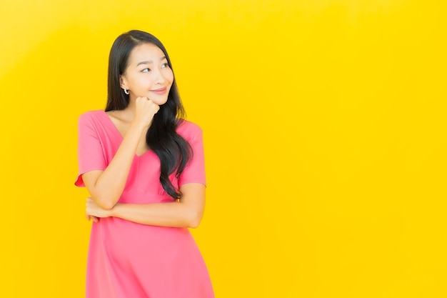 Retrato de joven y bella mujer asiática sonríe en vestido rosa en la pared amarilla