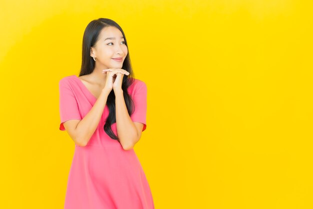 Retrato de joven y bella mujer asiática sonríe en vestido rosa en la pared amarilla