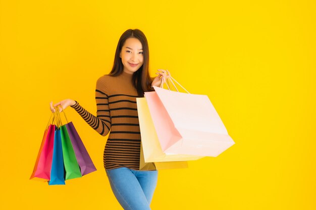 Retrato joven y bella mujer asiática sonrisa feliz con una gran cantidad de bolsas de color de los grandes almacenes en la pared amarilla