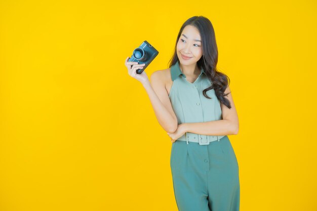 Retrato de joven y bella mujer asiática usa la cámara en la pared amarilla