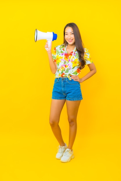 Retrato de joven y bella mujer asiática utiliza megáfono para comunicarse en la pared amarilla