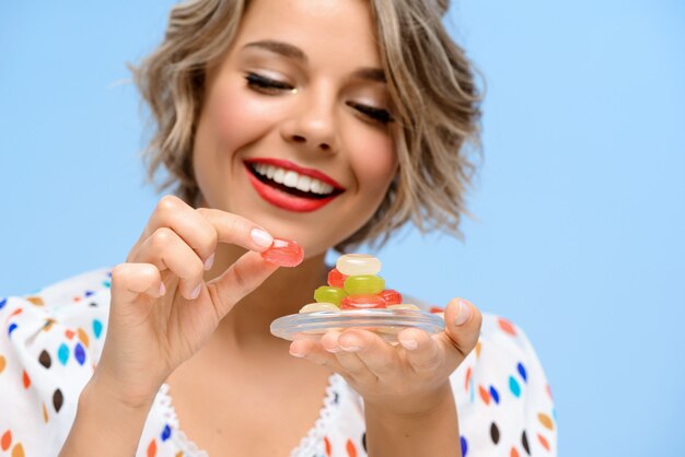 Retrato de joven bella mujer con dulces sobre pared azul