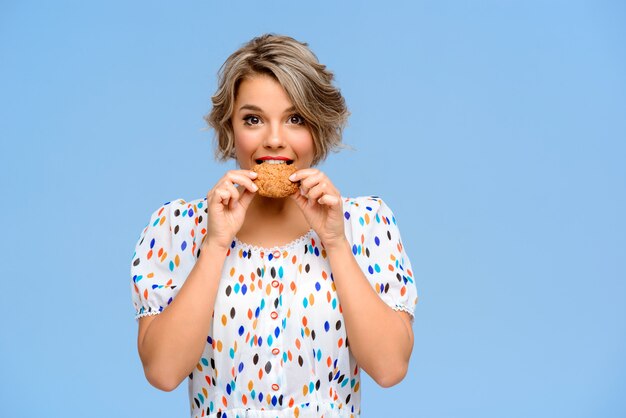 Retrato de joven bella mujer con dulces sobre pared azul