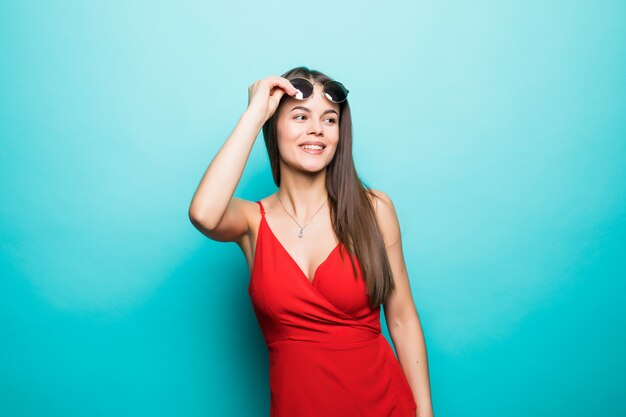 Retrato de joven bella mujer, elegante vestido rojo, tendencia de moda, con gafas de sol en la pared azul