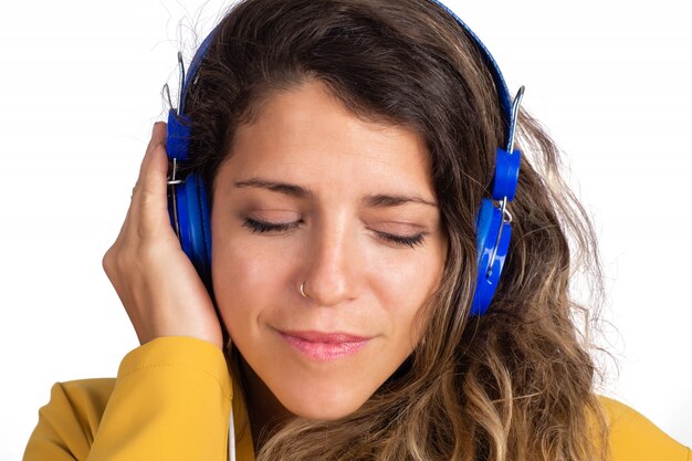 Retrato de joven bella mujer escuchando música con auriculares azules en estudio.