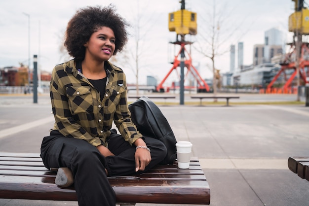 Foto gratuita retrato de joven y bella mujer latina afroamericana con pelo rizado sentado al aire libre en la calle.