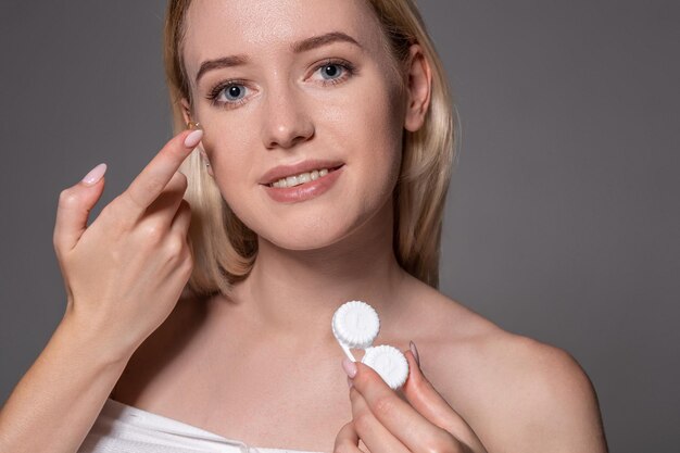 Retrato de joven bella mujer con maquillaje natural y lentes de contacto en la mano. Primer plano de modelo femenino con caja de lente blanca. Cuidado de los ojos y estilo de vida saludable. Salud de los ojos.