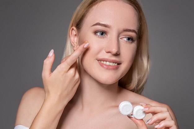 Retrato de joven bella mujer con maquillaje natural y lentes de contacto en la mano. Primer plano de modelo femenino con caja de lente blanca. Cuidado de los ojos y estilo de vida saludable. Salud de los ojos.