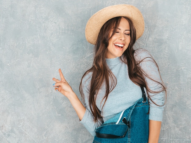 Retrato de joven bella mujer mirando. Chica de moda en ropa casual de verano y sombrero ... Muestra el signo de la paz