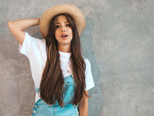 Retrato de joven bella mujer mirando. Chica de moda en ropa de verano casual monos y sombrero.