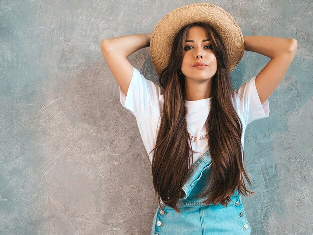 Retrato de joven bella mujer mirando. Chica de moda en ropa de verano casual monos y sombrero.