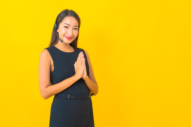 Retrato joven y bella mujer de negocios asiática con atención al cliente del centro de llamadas de auriculares sobre fondo amarillo