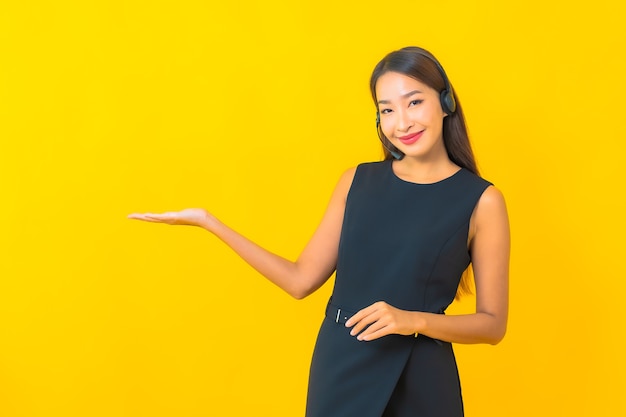 Retrato joven y bella mujer de negocios asiática con atención al cliente del centro de llamadas de auriculares sobre fondo amarillo