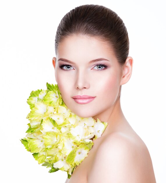 Retrato de joven bella mujer con una piel limpia y sana. Mujer bonita con flor cerca de la cara - aislada sobre fondo blanco.