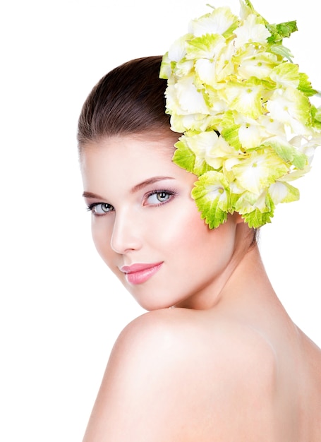 Retrato de joven bella mujer con una piel limpia y sana. Mujer bonita con flor cerca de la cara - aislada sobre fondo blanco.