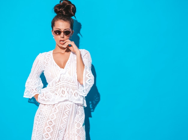 Retrato de joven bella mujer sexy con peinado ghoul. chica de moda en ropa de traje casual verano blanco hipster en gafas de sol. modelo caliente aislado en azul