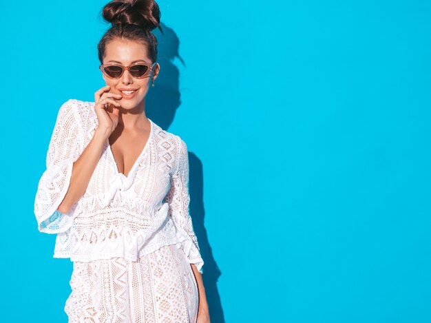 Retrato de joven bella mujer sexy sonriente con peinado ghoul. Chica de moda en ropa de traje casual verano blanco hipster en gafas de sol. Modelo caliente aislado en azul