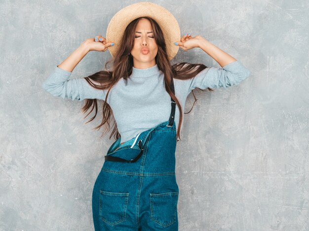 Retrato de joven bella mujer sonriente mirando. Chica de moda en ropa de verano casual monos y sombrero.