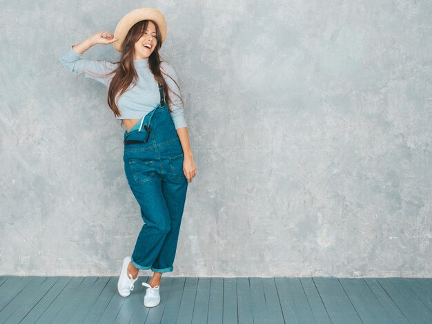 Retrato de joven bella mujer sonriente mirando. Chica de moda en ropa de verano casual monos y sombrero.