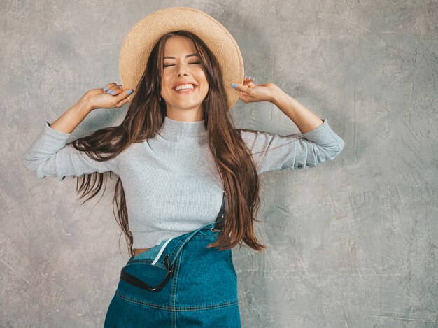 Retrato de joven bella mujer sonriente mirando. Chica de moda en ropa de verano casual monos y sombrero.