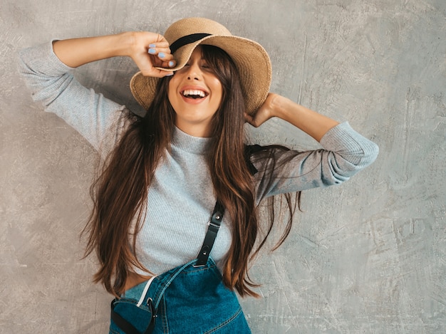 Retrato de joven bella mujer sonriente con los ojos cerrados. Chica de moda en ropa de verano casual monos y sombrero.