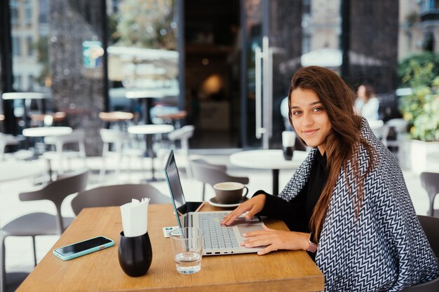 Retrato de una joven y bella mujer trabaja en una computadora portátil portátil, encantadora estudiante con net-book mientras está sentado en la cafetería